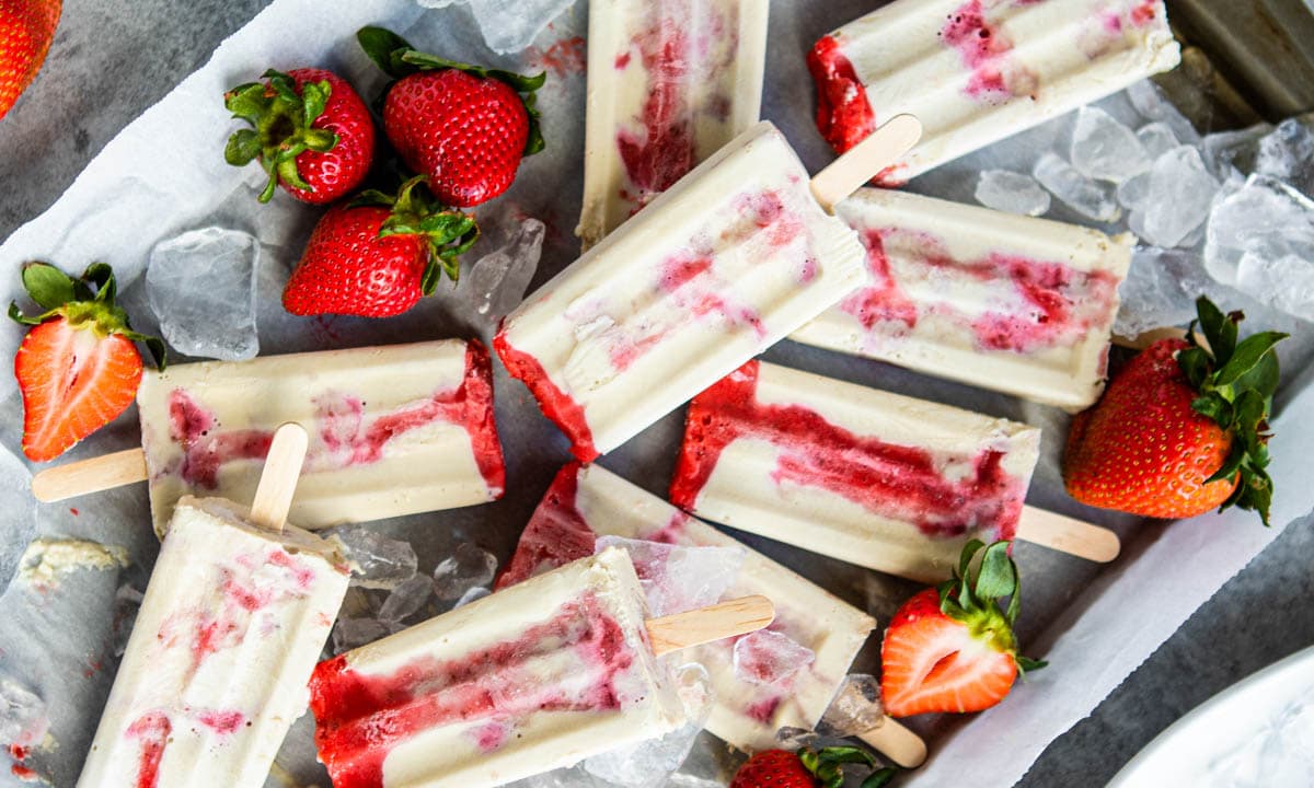 creamy strawberry popsicles on ice surrounded by fresh strawberries.