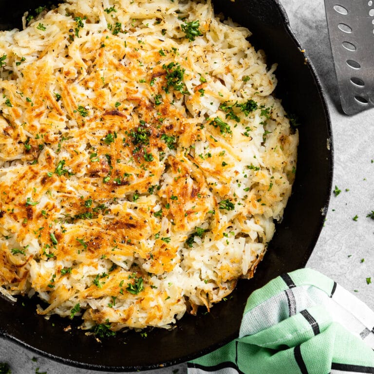 black skillet of crispy hash browns topped with fresh parsley.