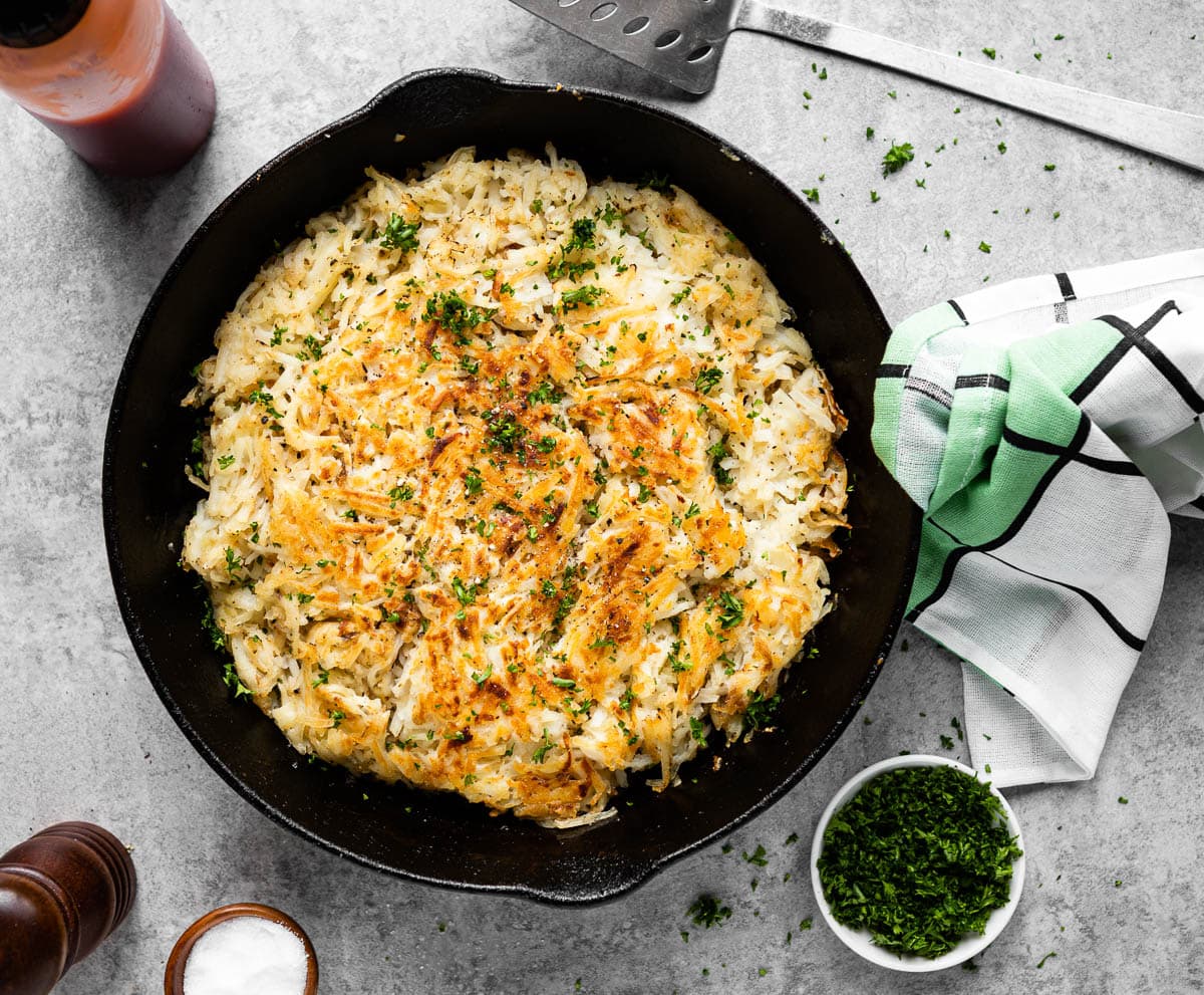 black skillet of restaurant-style hash browns topped with sea salt and fresh parsley.