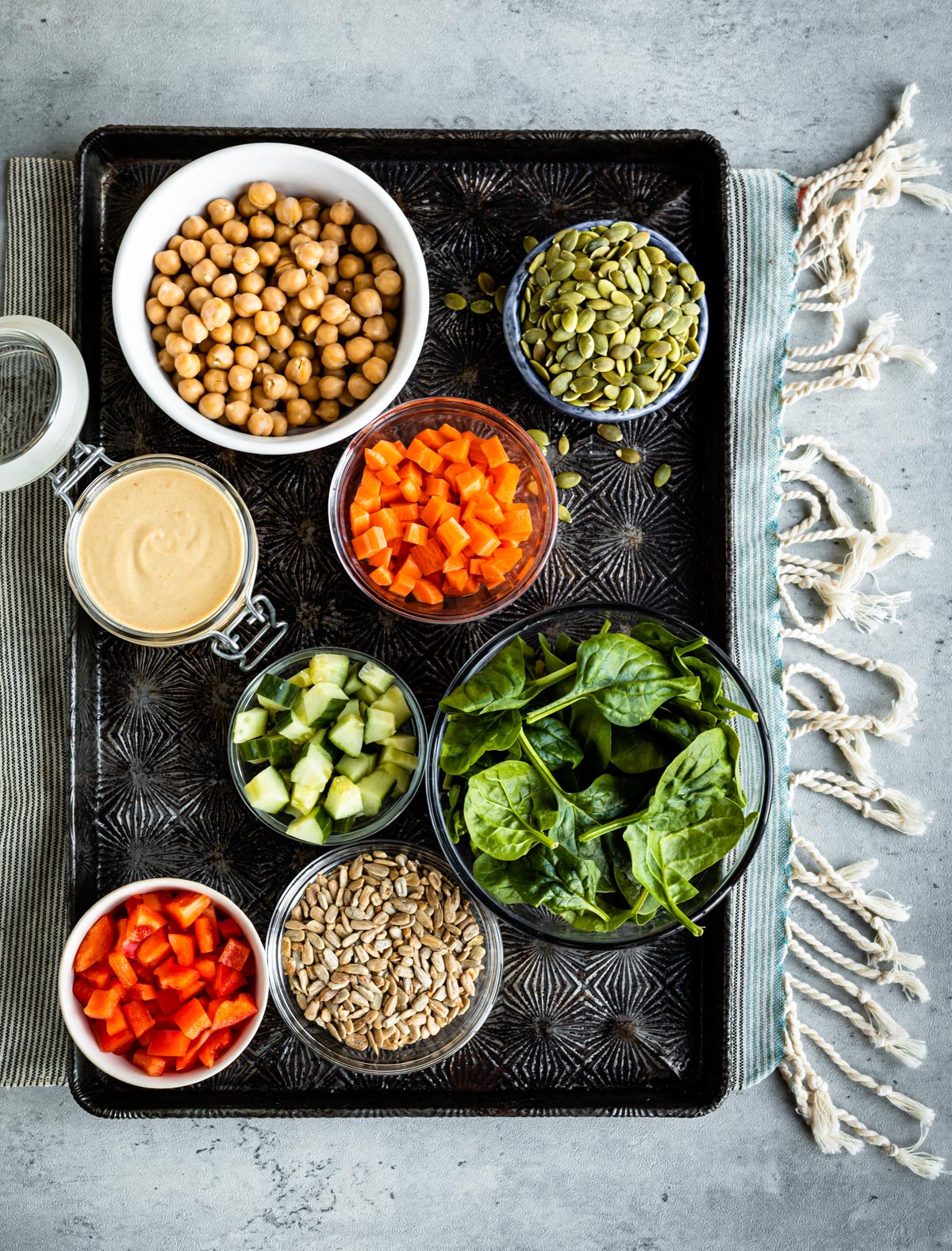 ingredients for a crunchy salad including chickpeas, pumpkin seeds, carrots, tahini dressing, spinach, cucumber, sunflower seeds and red pepper.