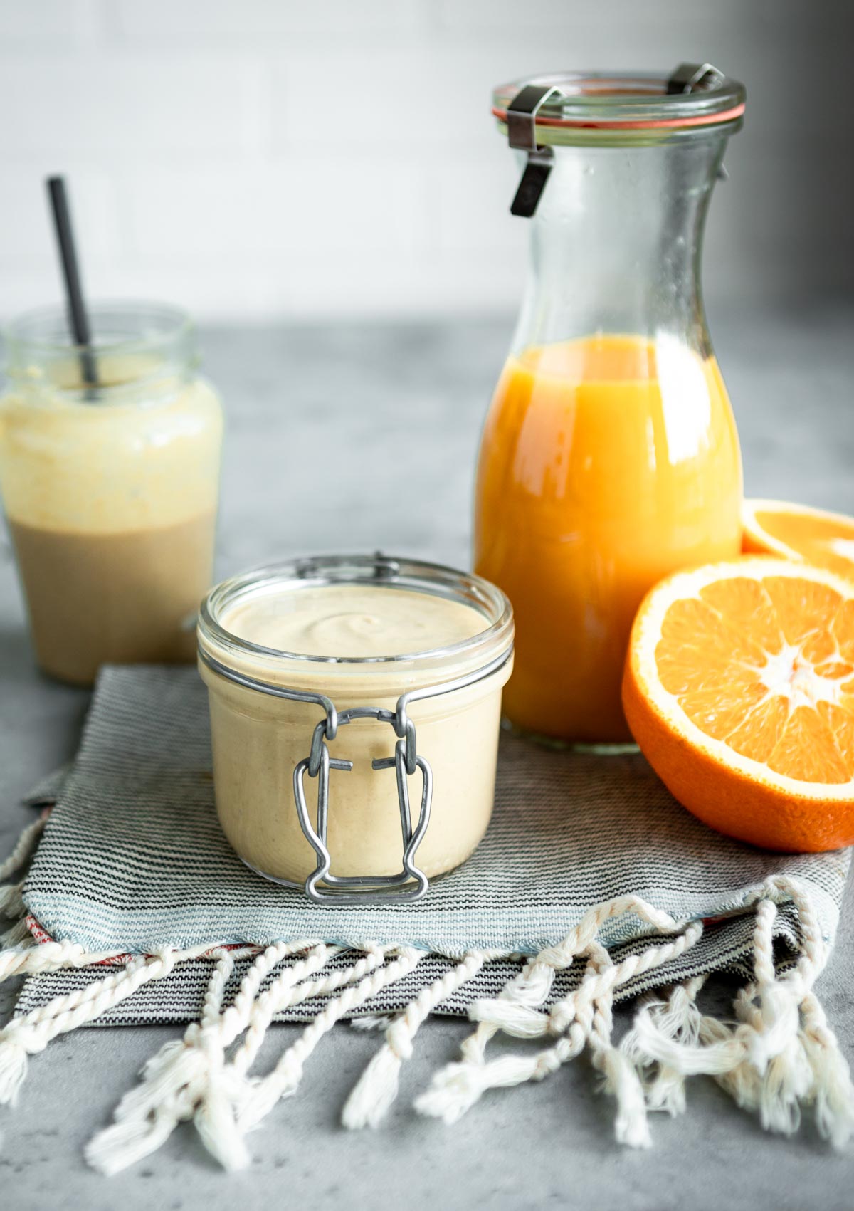 tahini dressing homemade in a glass jar next to oranges and fresh orange juice.