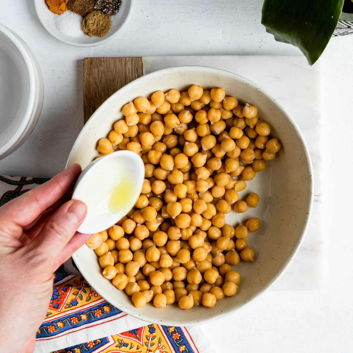 Pouring a small white bowl of olive oil onto a bowl of chickpeas.