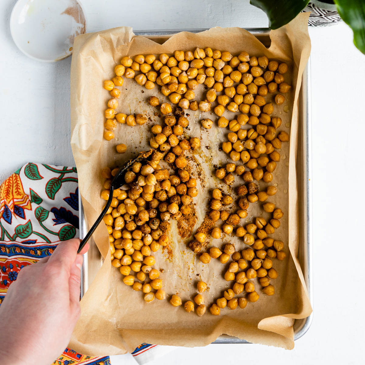 Sprinkling spices over a baking dish full of garbanzo beans.