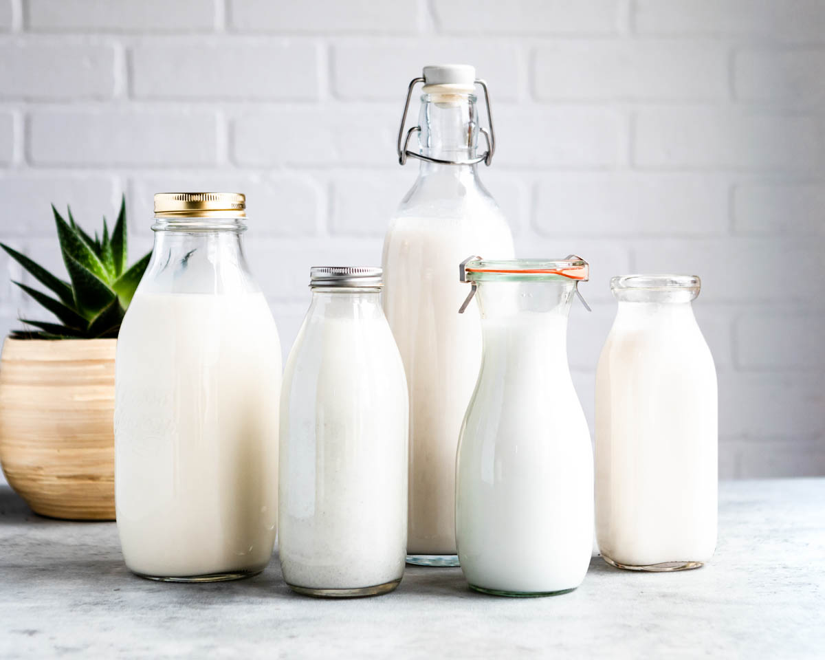 different kinds of vegan 'milk' in glass jars on a counter.