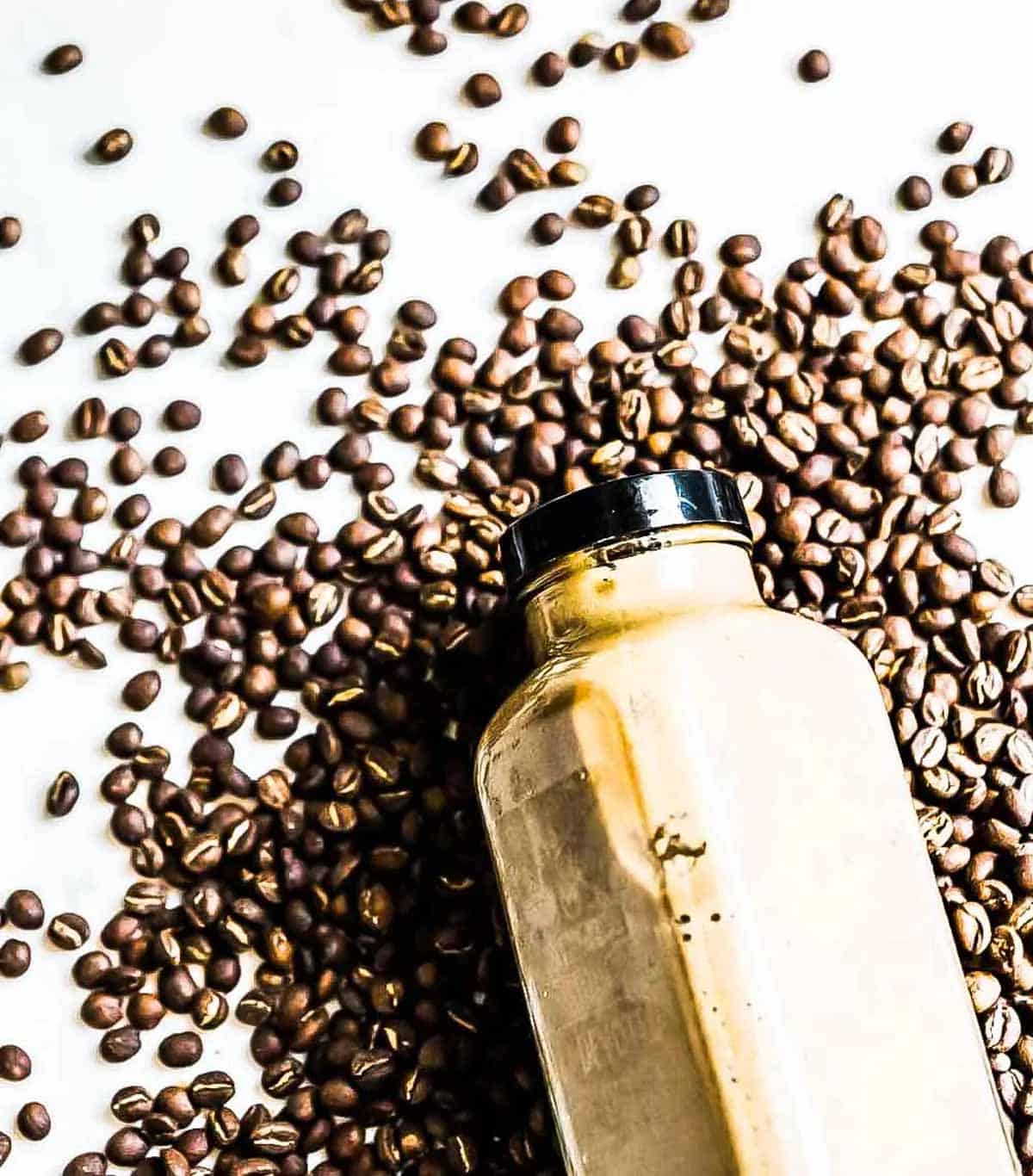 brown smoothie in a glass jar with a black lid on a bed of coffee beans with no dairy in it.