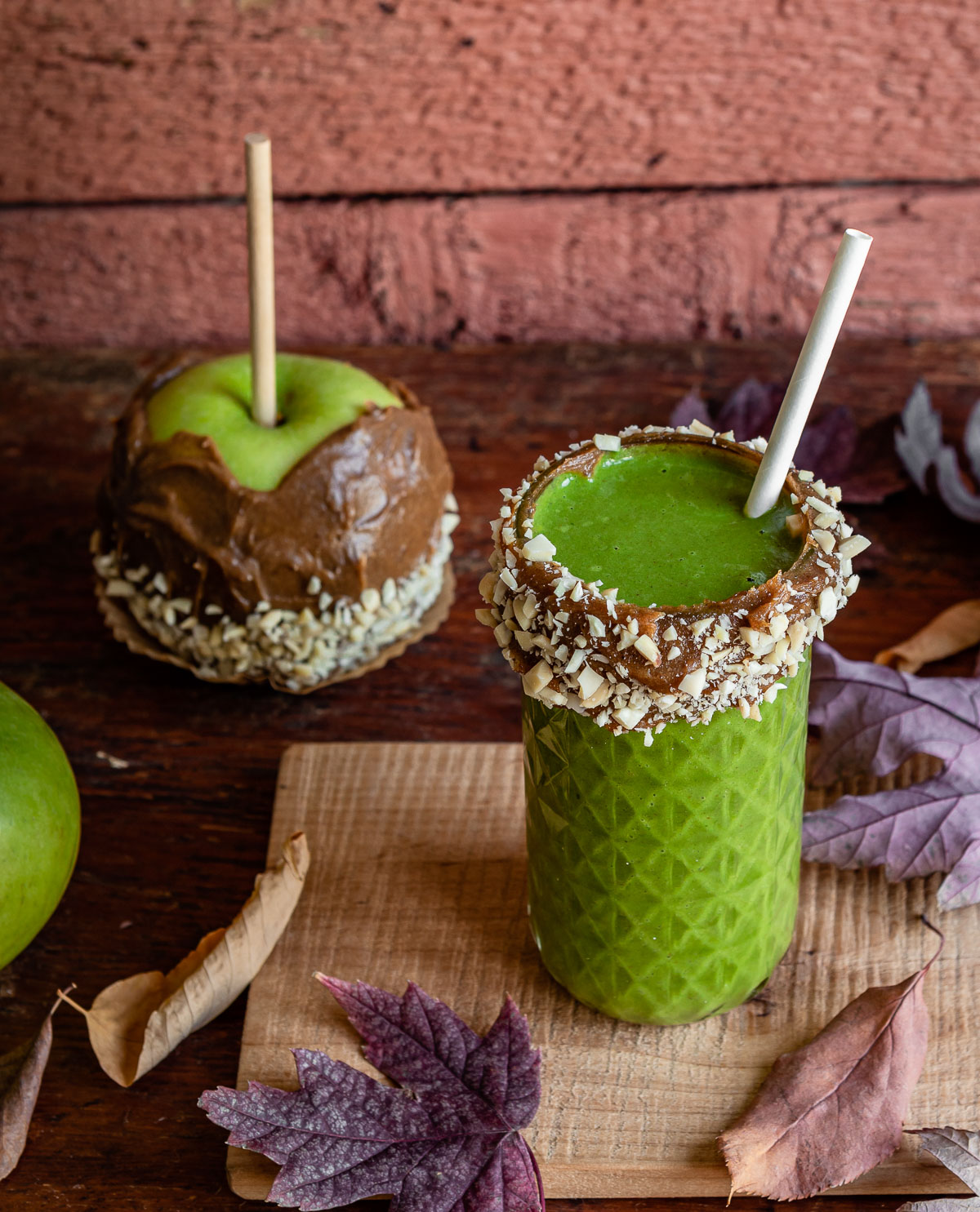 Glass of green smoothie with date caramel and nut-crusted rim, paired with a nut-covered date caramel apple