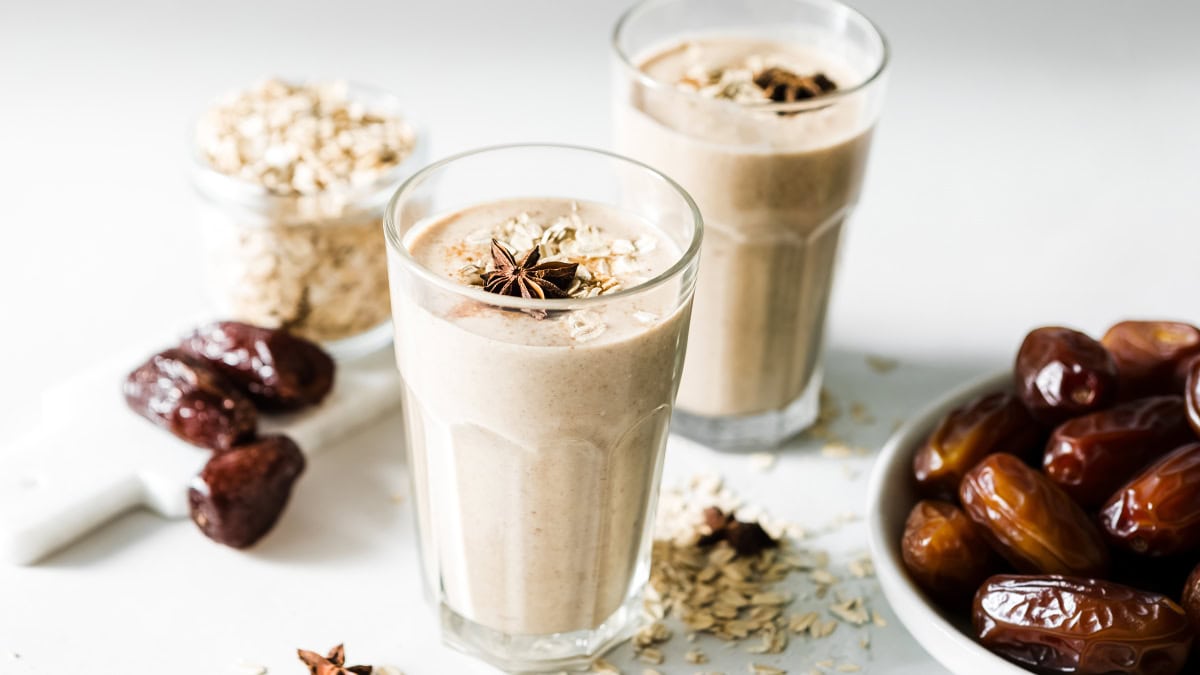 Creamy cinnamon date smoothie in a glass with star anise and oats on a white background.