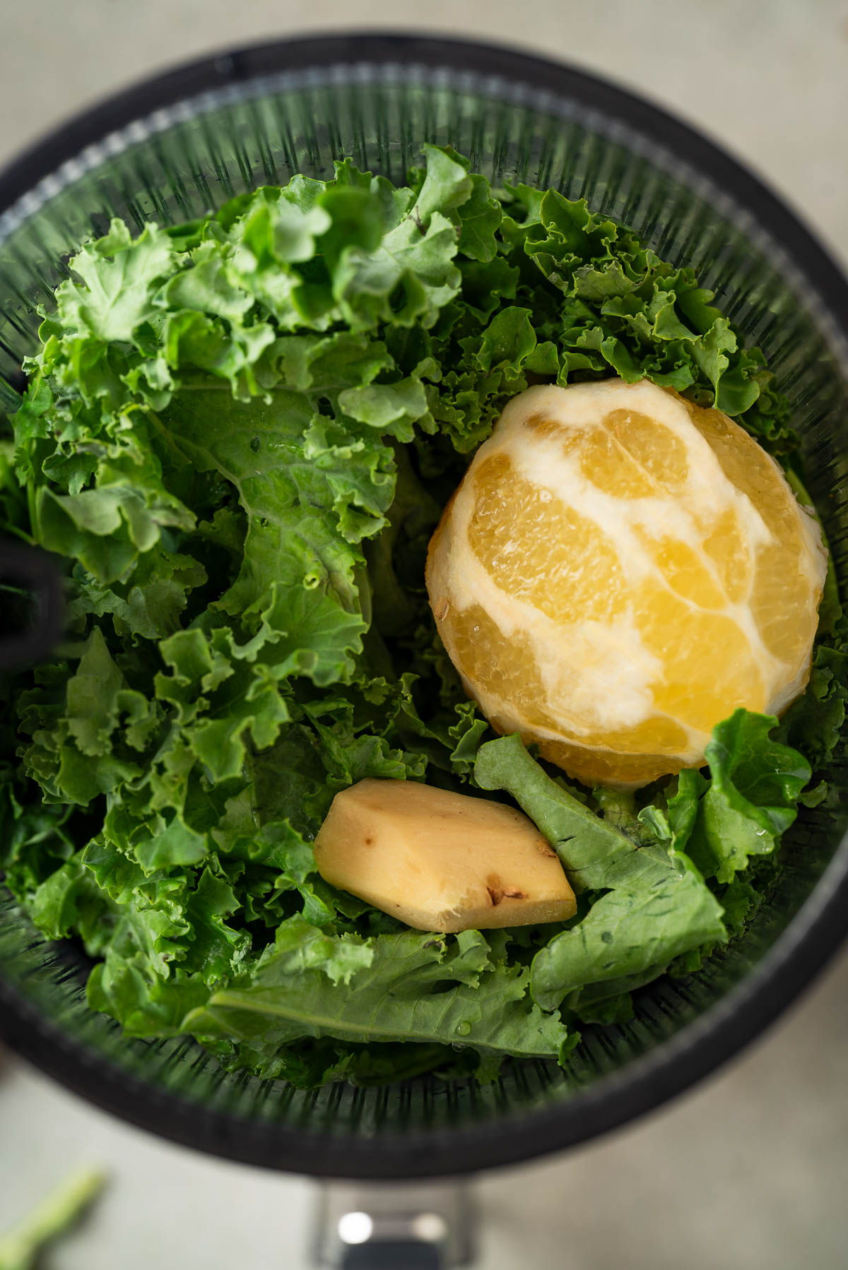 A peeled lemon, ginger, and kale in a juicer