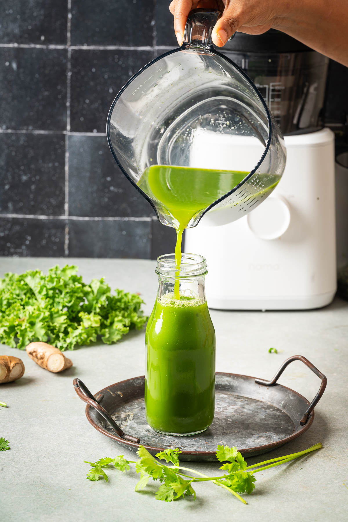 A person pouring green juice in a glass bottle