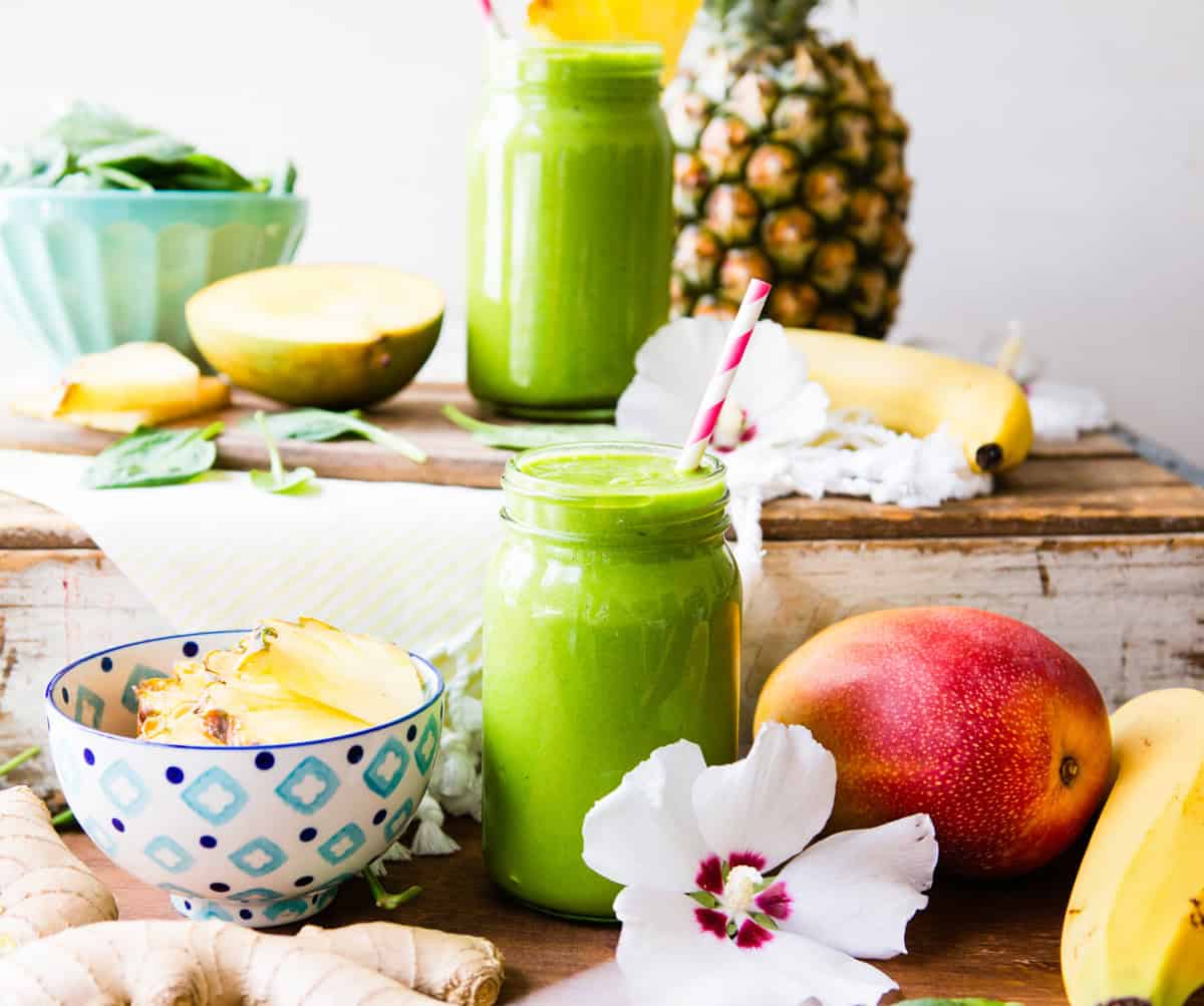 Healthy green smoothie in a jar with tropical fruits and flowers on a rustic table.