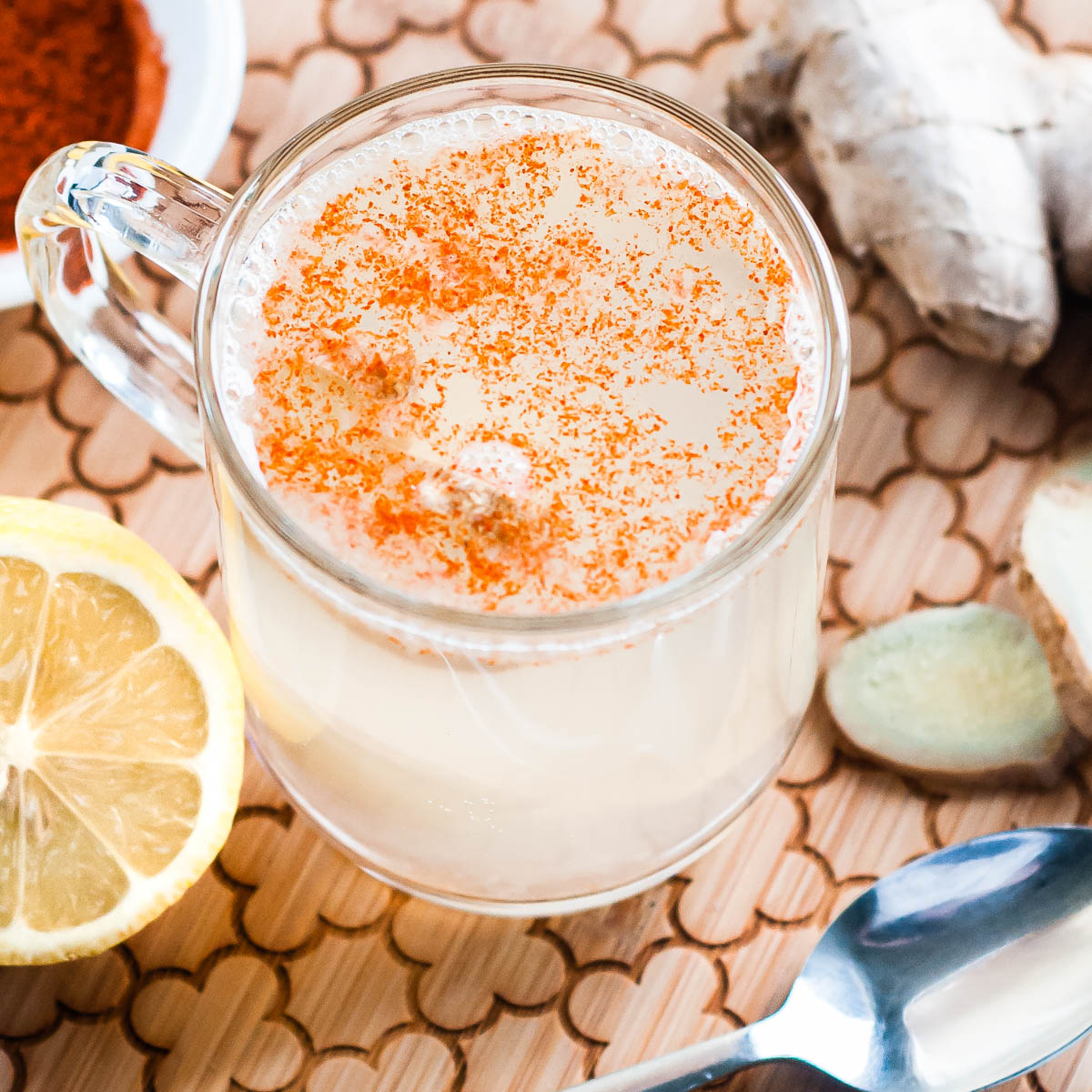 white cloudy liquid in a glass mug sprinkled with cayenne pepper with a spoon and ginger root.