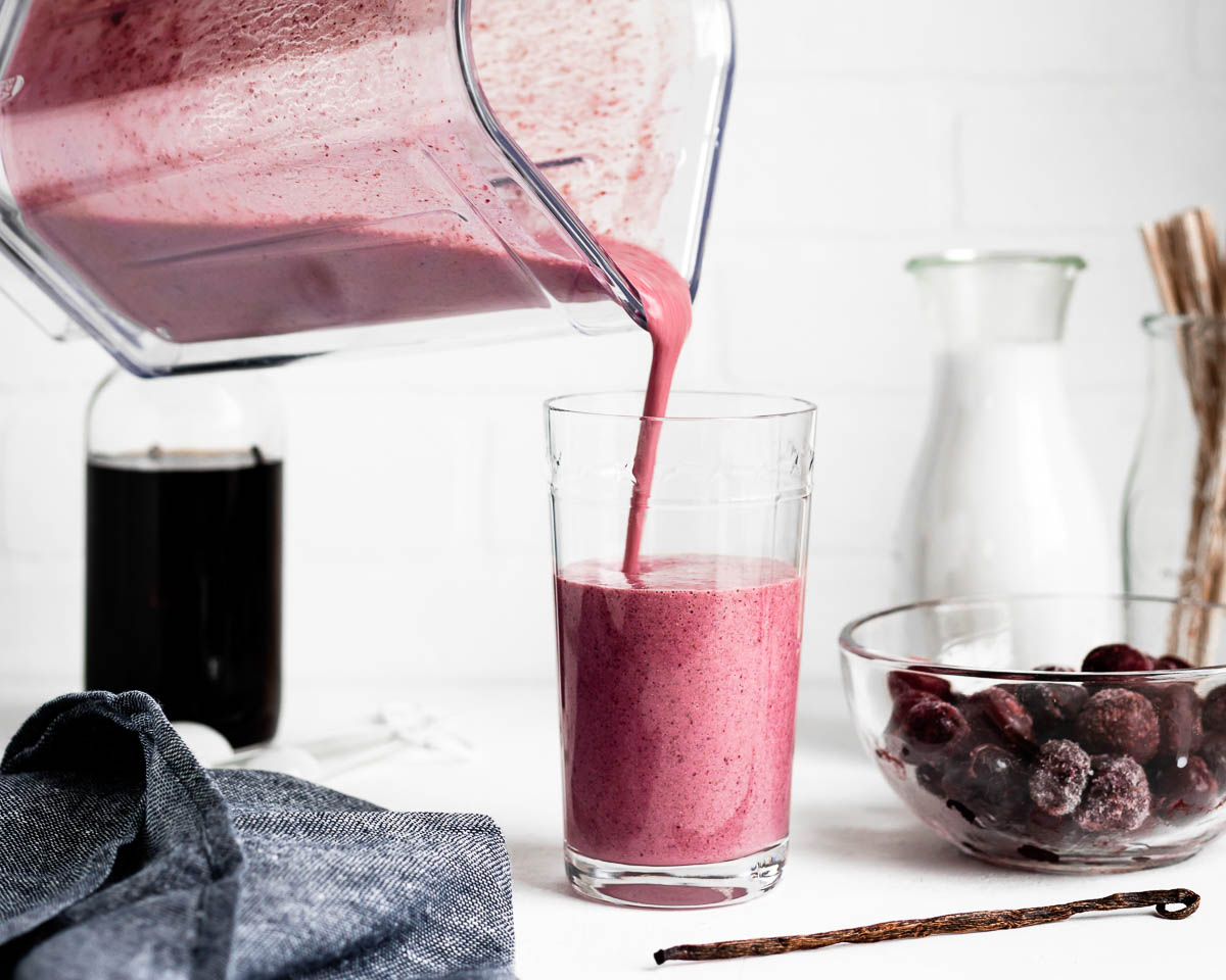 pouring a pink smoothie into a tall glass on a white counter top.