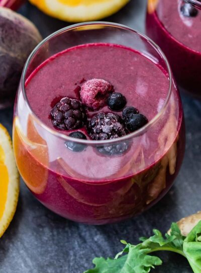 glass with purple smoothie in it, topped with frozen fruit.