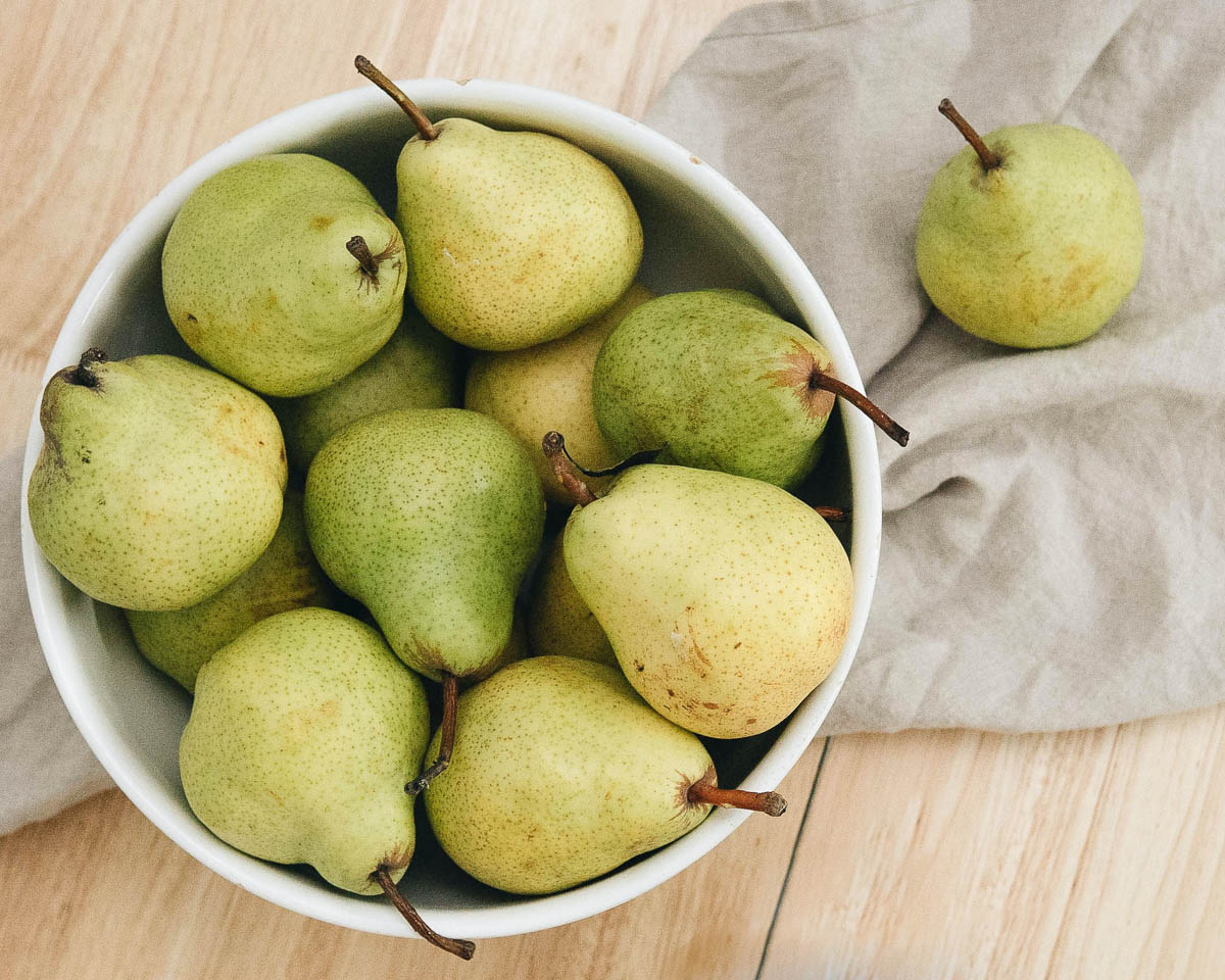 white bowl of green pears on a tea towel.