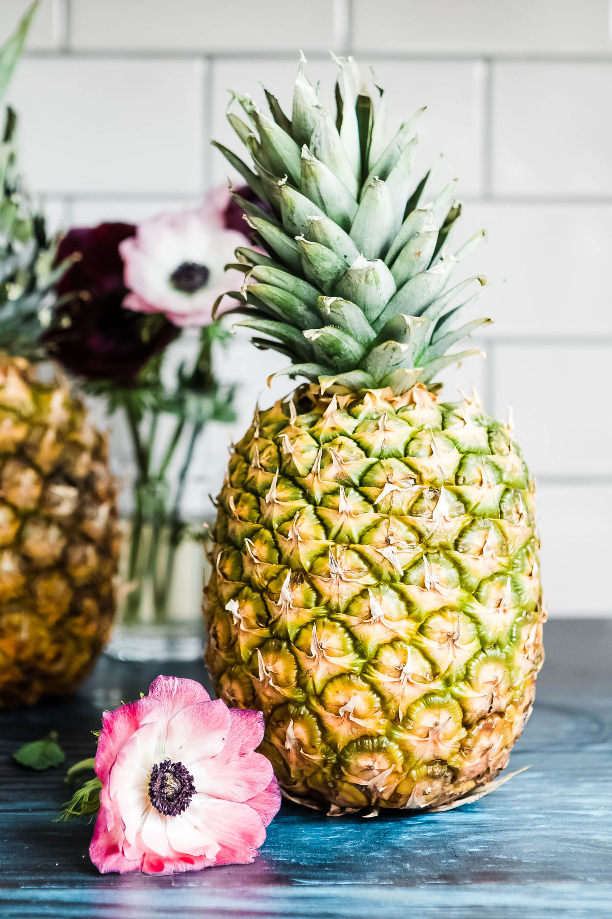 whole pineapple on a countertop next to a pink flower.