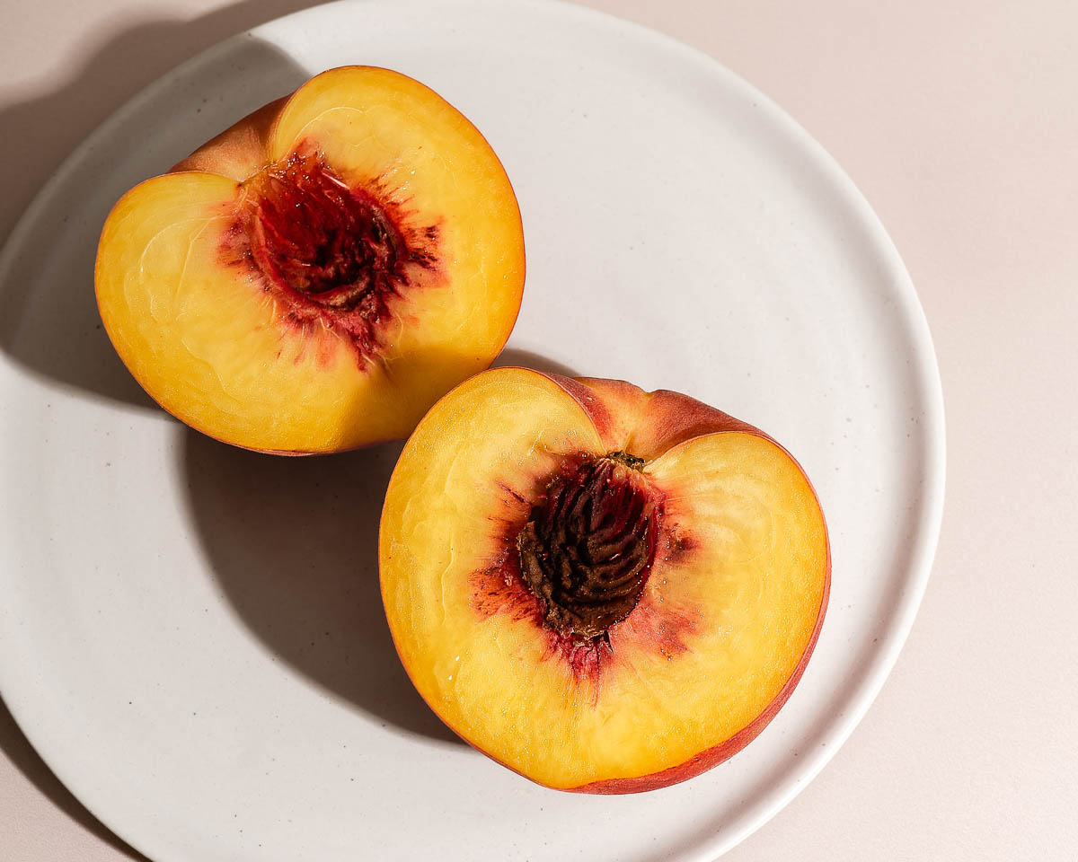 white plate with peach cut in half to reveal pit.