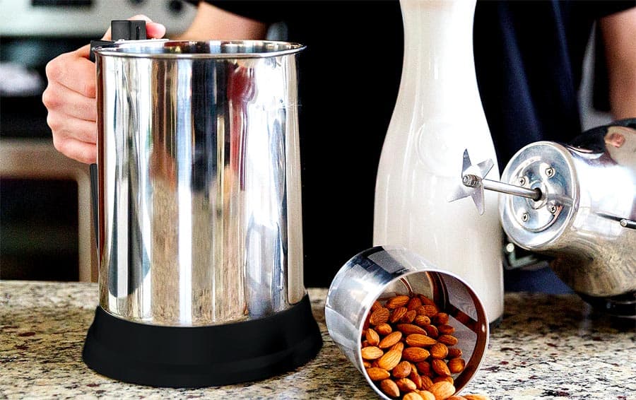 Making plant-based milk with the Almond Cow, next to a jar full of milk and a stainless steel container of raw almonds.