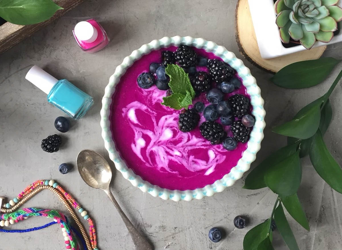 pink and blue nail polish next to a dragon fruit bowl with berries and fresh mint.