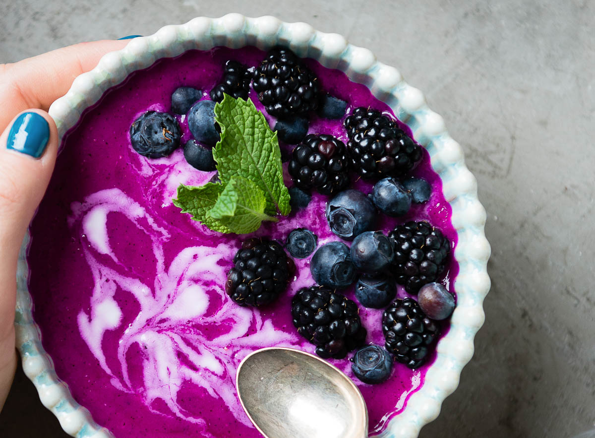 purple dragon fruit smoothie bowl swirled with white coconut whipped cream and topped with berries and fresh mint.