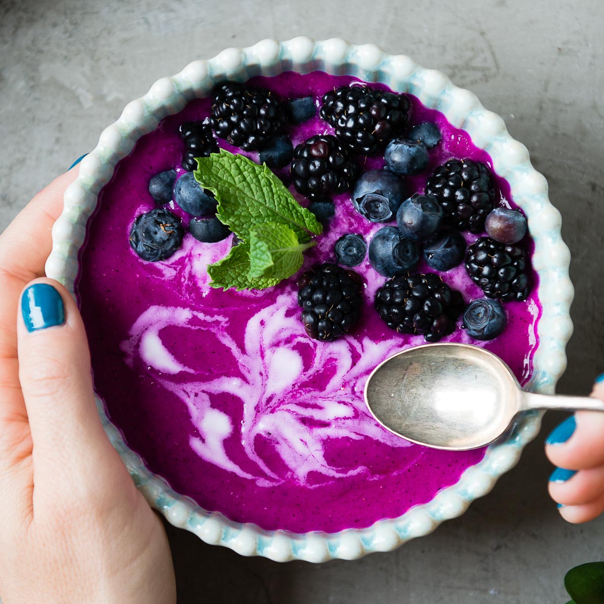 Person using a spoon over a dragon fruit smoothie bowl.
