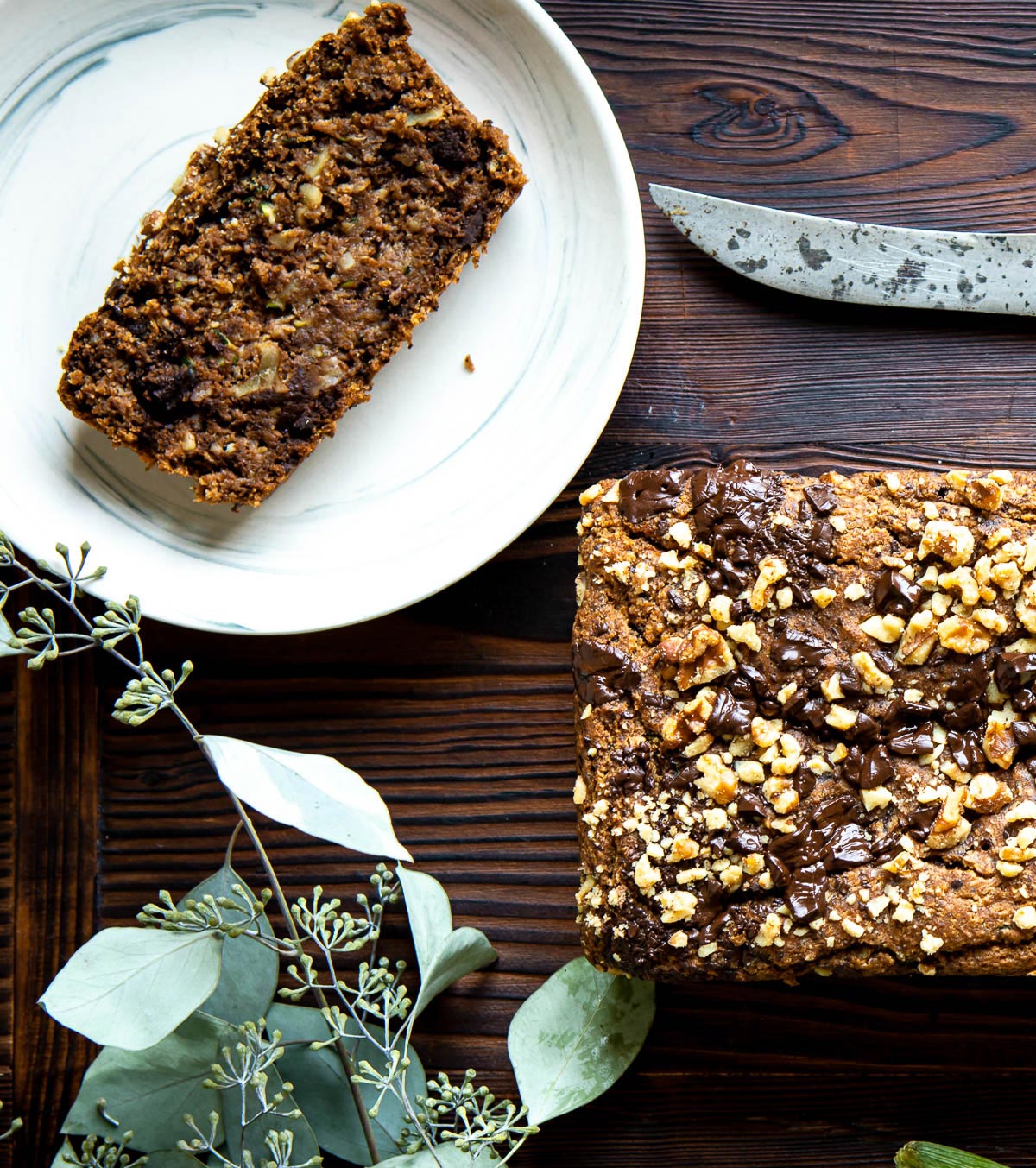 Slice of zucchini bread on a plate next to the rest of the loaf.