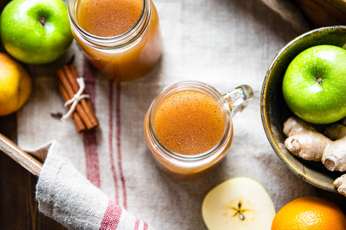 Glass jars of crockpot apple cider topped with spices. 