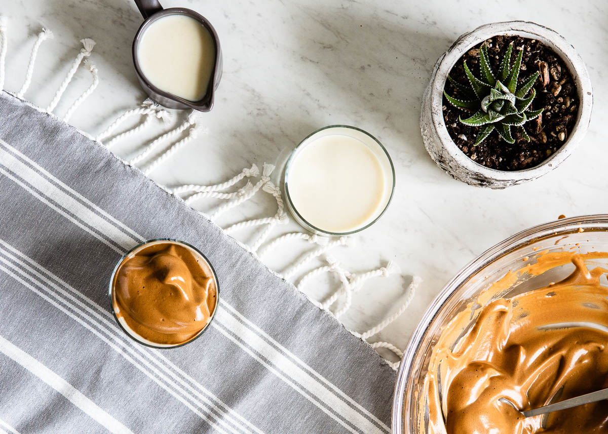 glass of topped whipped coffee and glass of warm plant-based milk ready for topping.