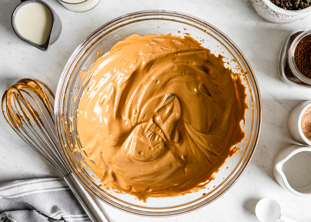 brown whipped mixture in a glass bowl next to a whisk.