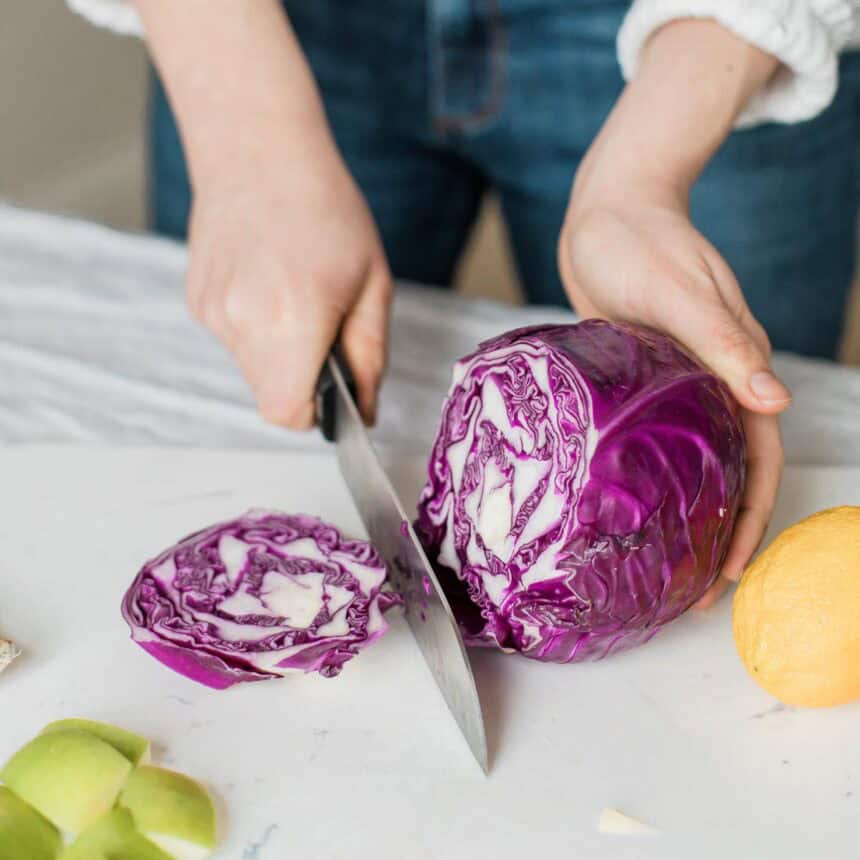 chopping a whole purple cabbage with a black chef's knife.