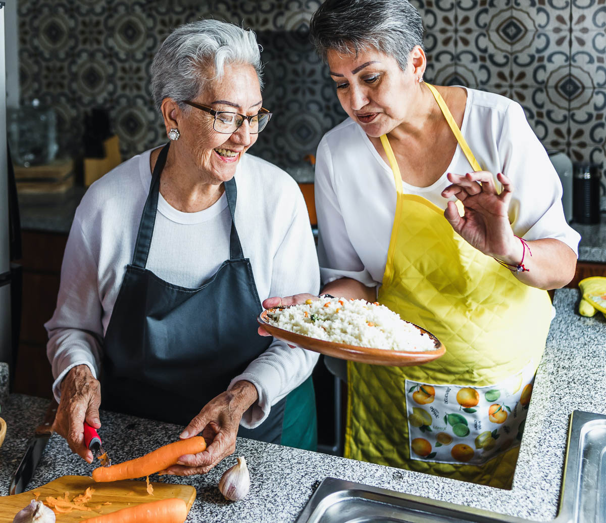 two women in aprons looking at a large serving bowl of rice.