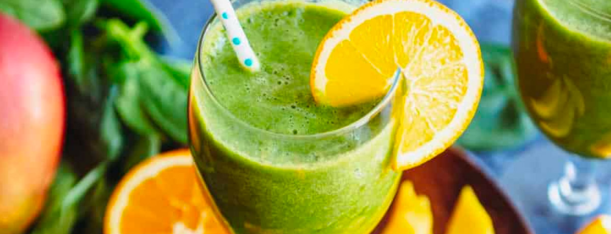 green smoothie in a glass with an orange wedge on the rim and a straw