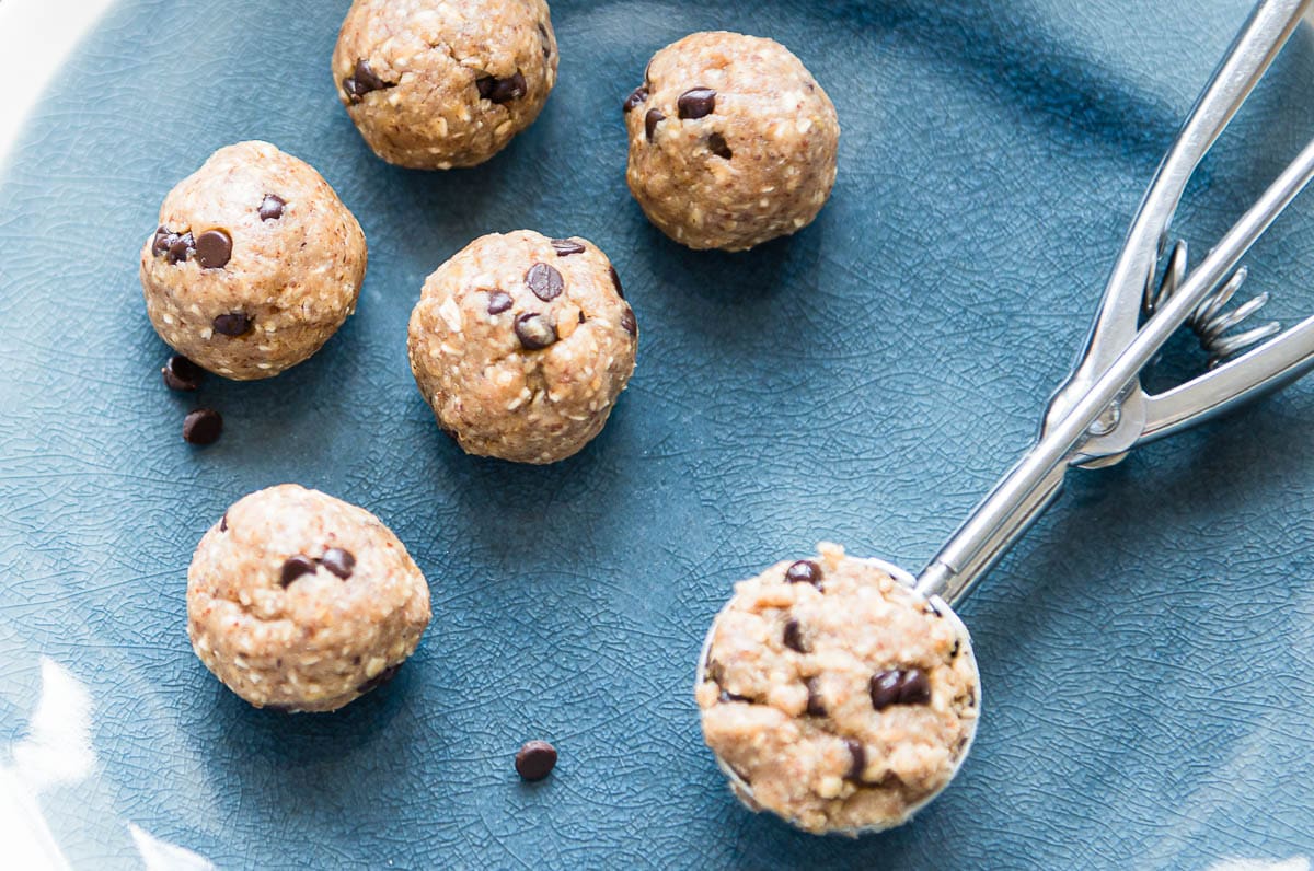 deliciously healthy no-bake snack that tastes like chocolate chip cookies on a blue plate with a cookie scoop.