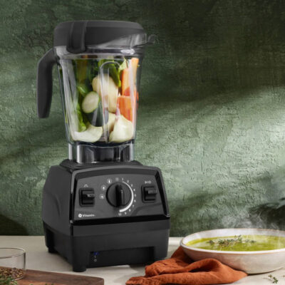 Vitamix explorian blender in kitchen with bowl of green soup.