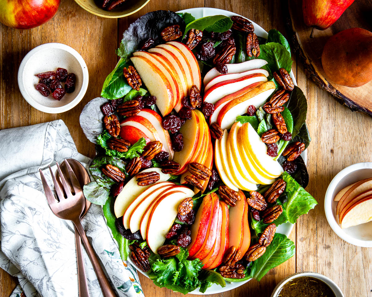 platter of fall salad featuring a bed of mixed greens topped with sliced apples, pears, candied pecans, dried cherries and a vinaigrette.