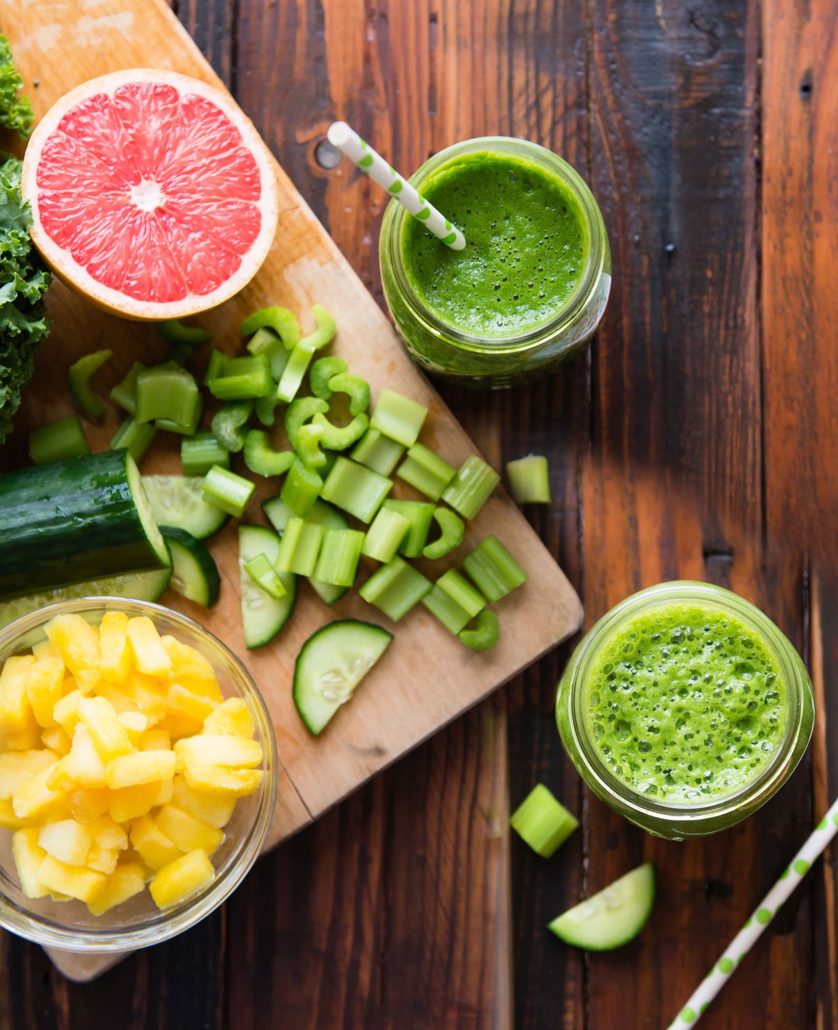 Celery and cucumber cut up next to grapefruit, pineapple and two glasses of smoothies for weight loss.