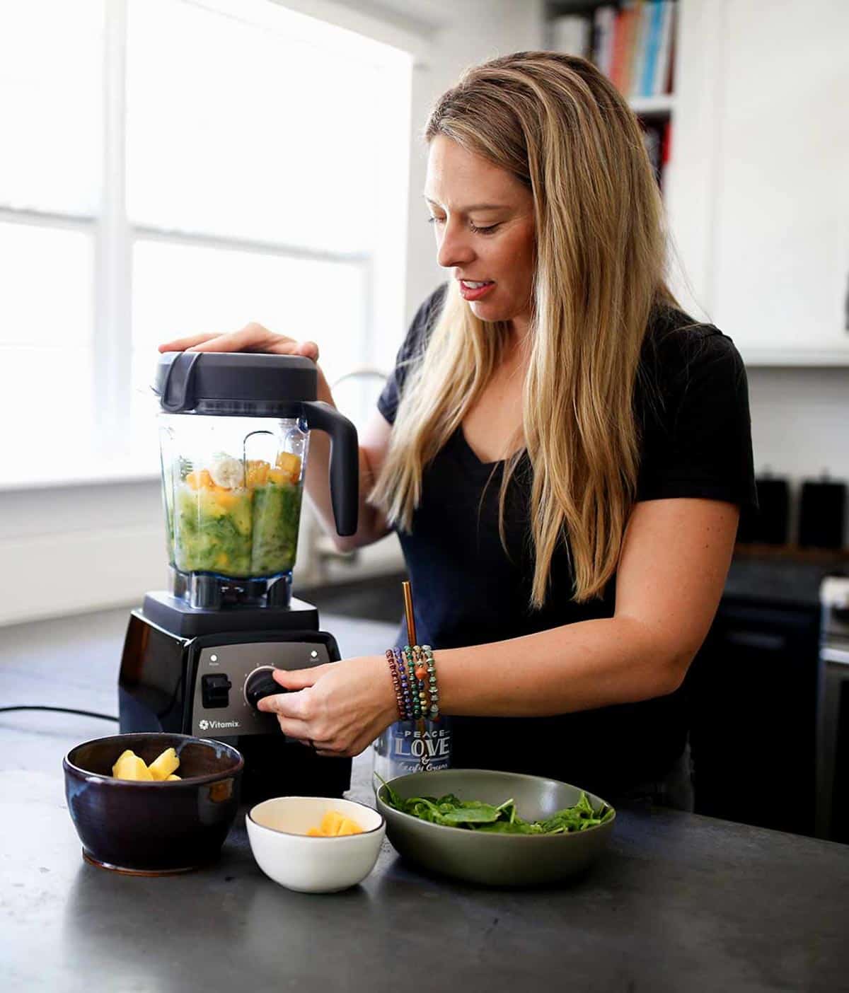 A blond woman blending weight loss smoothies in her kitchen on concrete countertop.