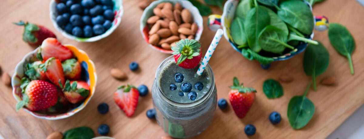 top down view of a smoothie in a jar, bowl of almonds, bowl of blueberries, bowl of strawberries, and bowl of spinach
