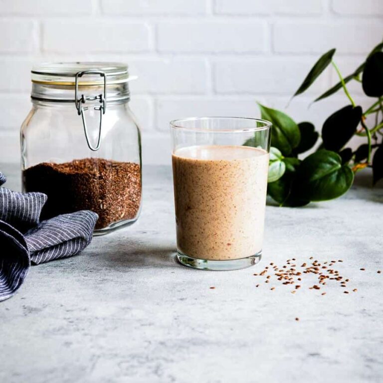 flaxseed smoothie in a glass next to a jar of flaxseeds.