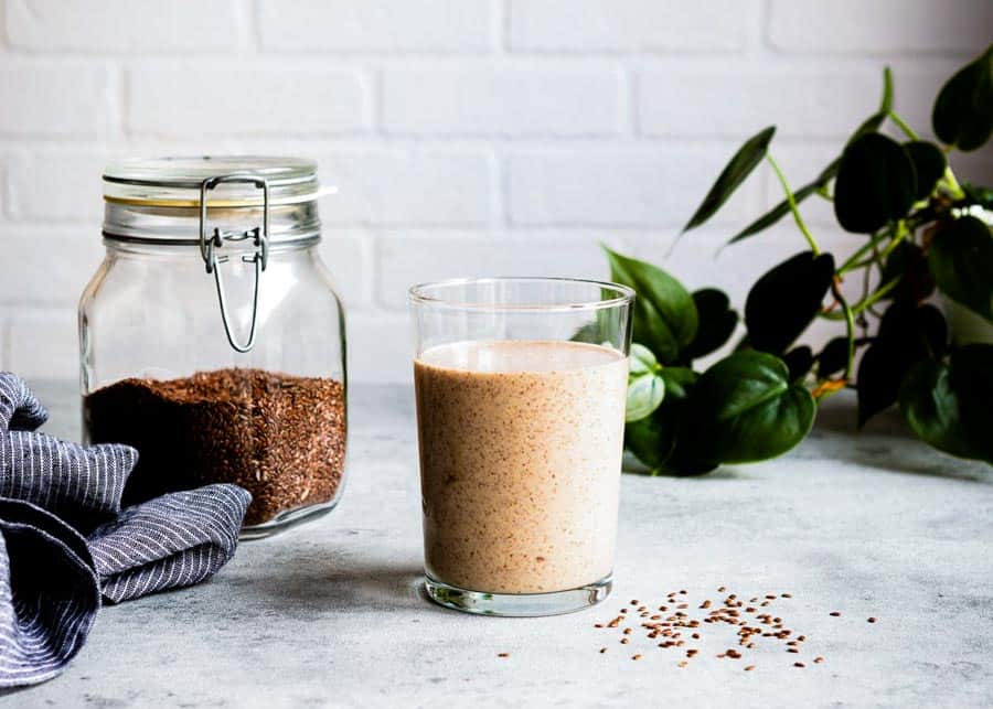 flaxseed smoothie in a glass next to a jar of flaxseeds.