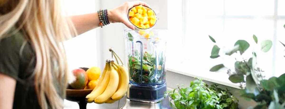 woman pouring ingredients into a blender to make a green smoothie