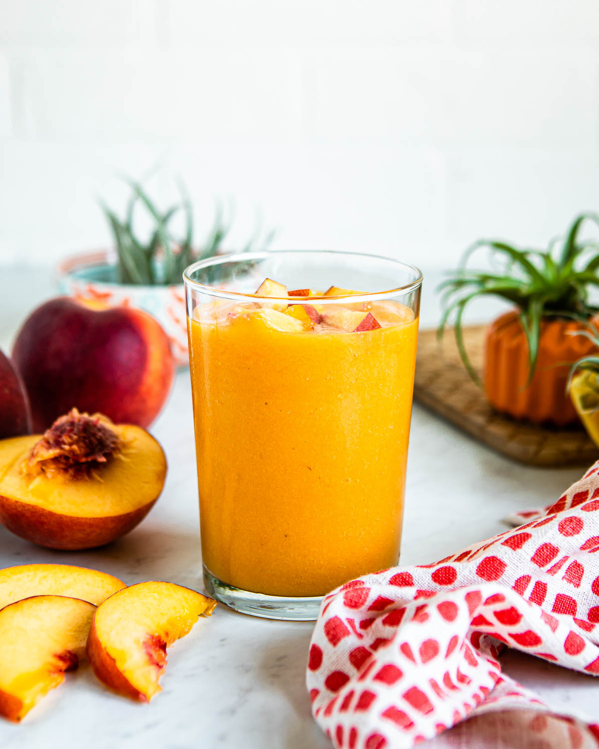 peach smoothie in a glass on a white countertop surrounded by fresh peaches.