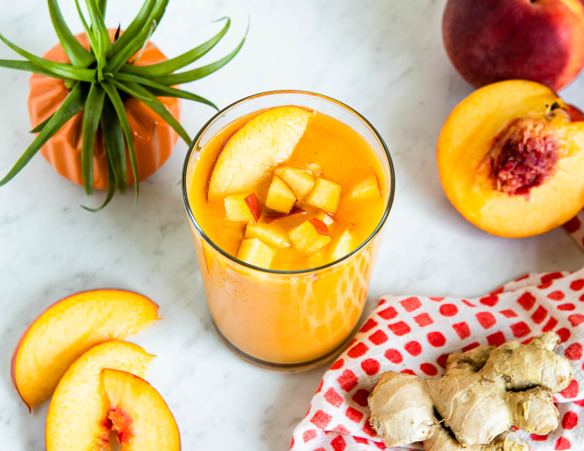 orange smoothie in a glass topped with fresh fruit on a white countertop.