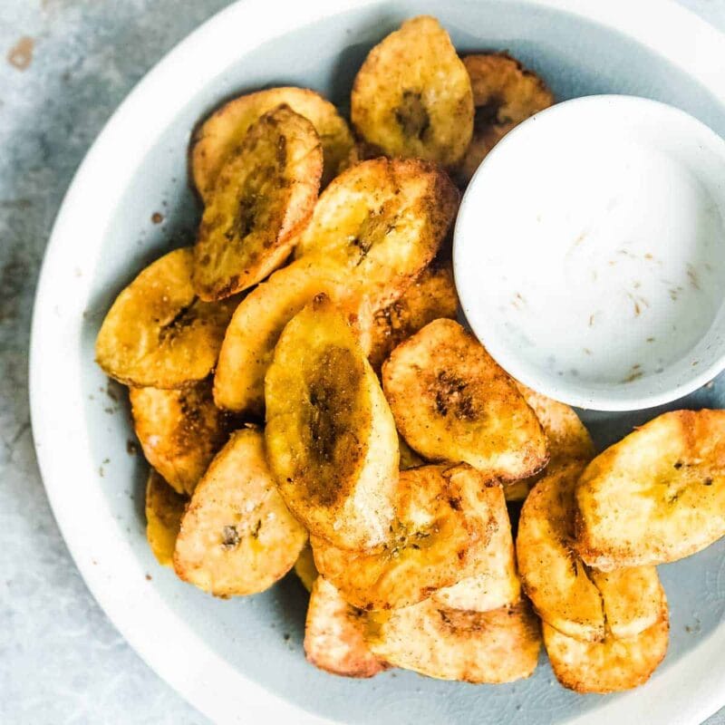 fried plantains on a plate with a bowl of dipping sauce.