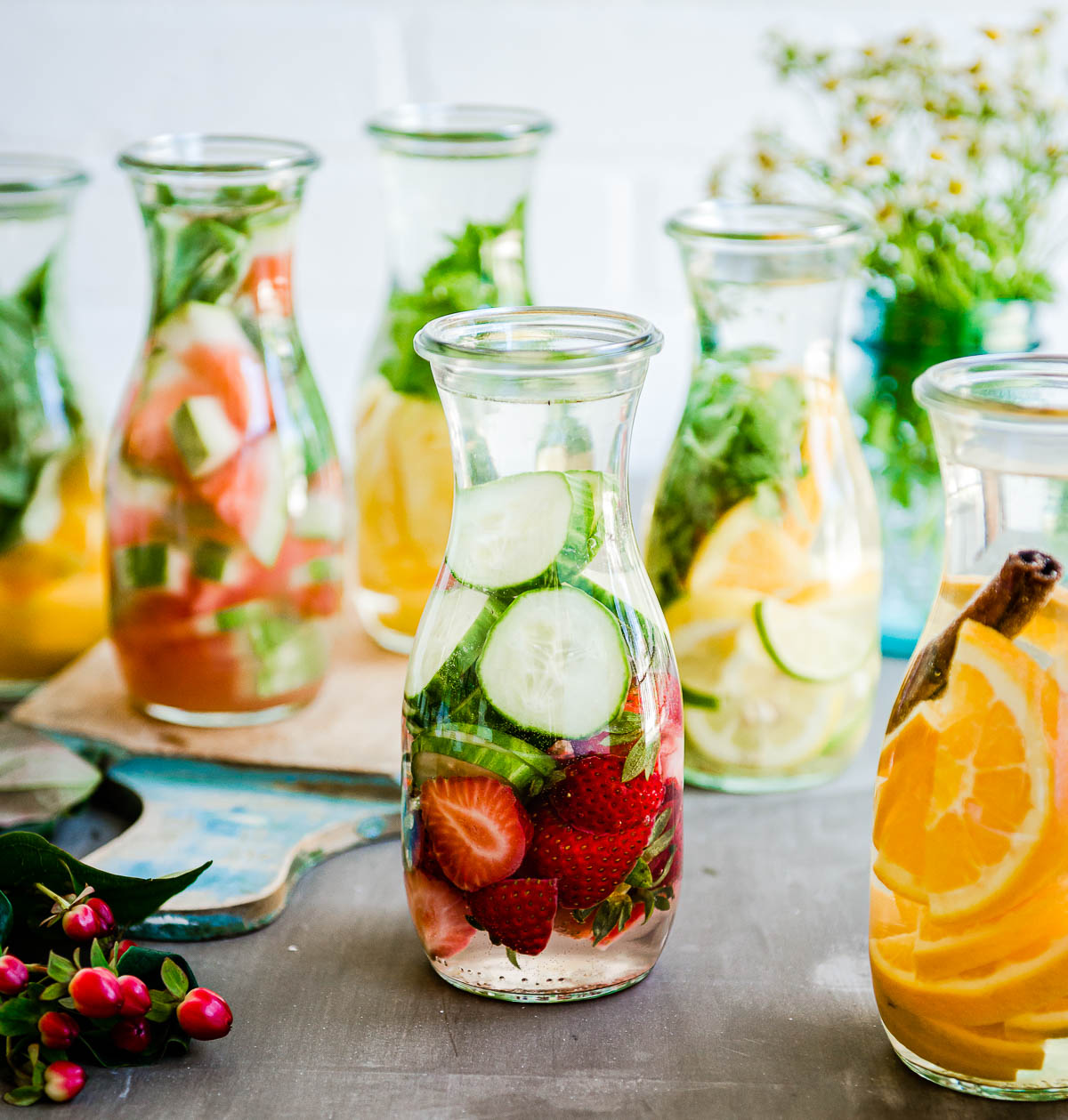 several liter jars of fruit-infused waters including one with cucumber and strawberries in the middle.