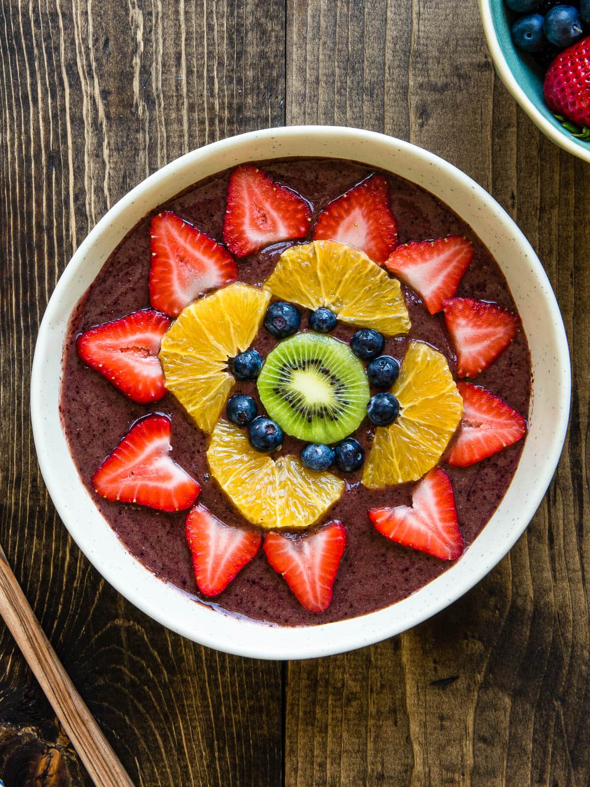 bowl full of smoothie and topped with strawberries, oranges, blueberries and kiwi.