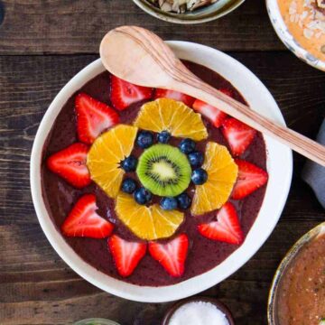 overhead photo of a fruit smoothie bowl topped with fresh fruit and a wooden spoon
