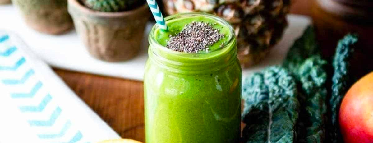 green smoothie in a jar with chia seeds sprinkled on top and a blue and white striped straw