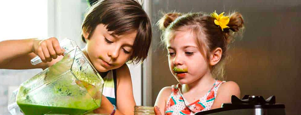 two kids pouring green smoothies into jars with green smoothie mustaches