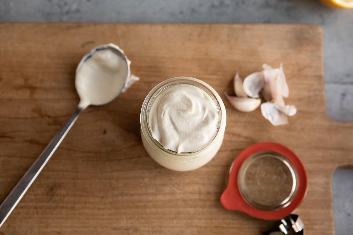 vegan dressing using cashews in glass jar with stainless spoon and garlic cloves.