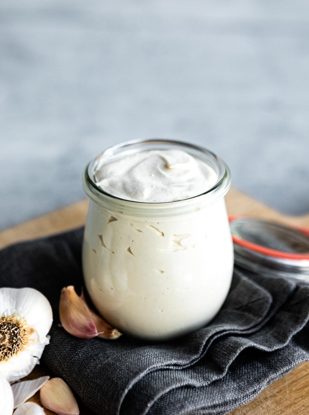 simple vegan aioli in a glass jar next to cloves of garlic.